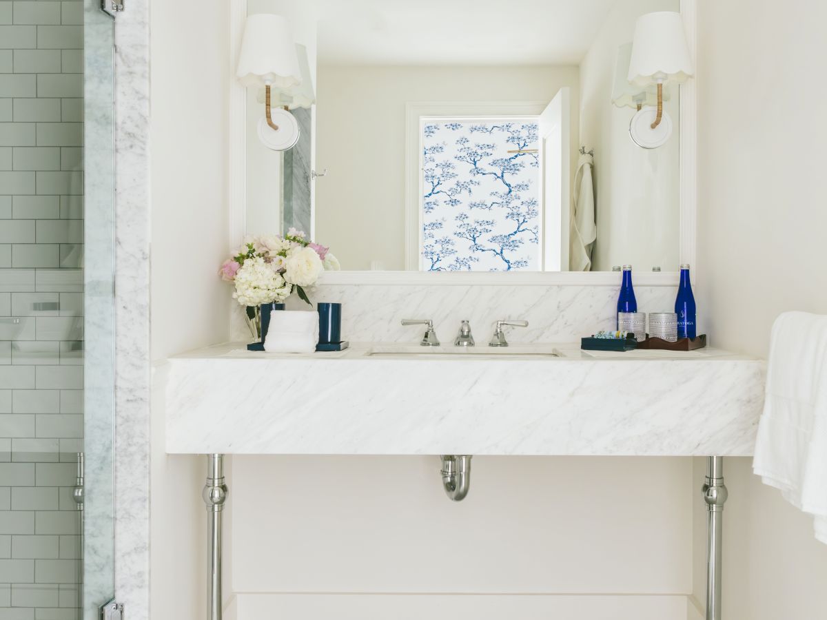 A clean, modern bathroom with a large mirror above a white vanity, two wall-mounted lights, a glass shower, and a towel rack.