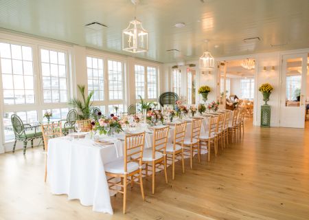 The image shows an elegantly decorated dining room with a long table set for a formal gathering. The room has large windows and light wooden floors.