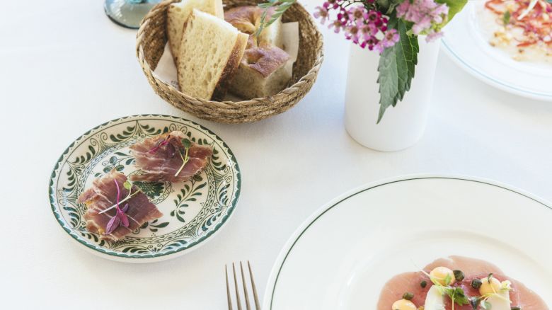 The image shows an elegant table setting with a plate of appetizers, a basket of bread, and a vase with flowers, likely for a meal.